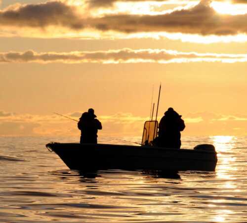 To mennesker i en liten båt på havet som fisker under midnattssolen