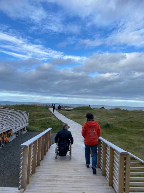 Rullestolrampe ved havet med gående og rullestolbruker.