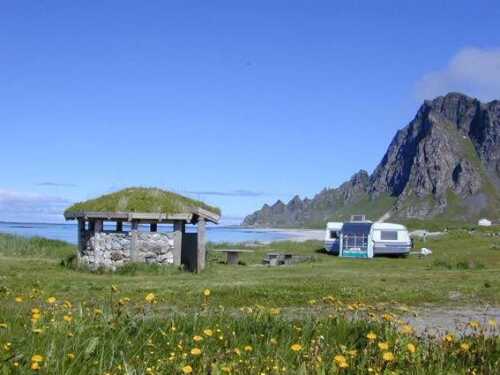 Grillhytte og bobil på campingplass med utsikt mot hav og fjell.