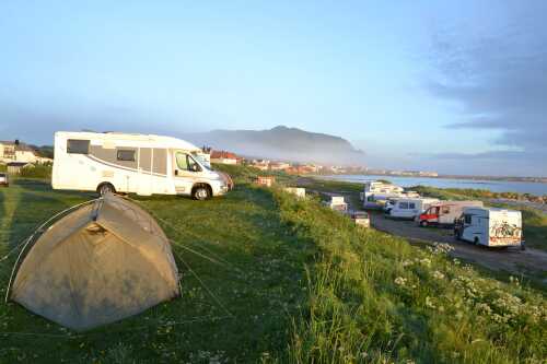 Morgensol på campingplass med telt og bobiler.