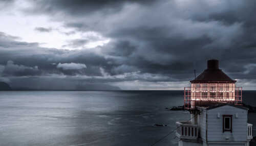 Opplyst Litløy fyr, blank sjø og dramatiske skyer.